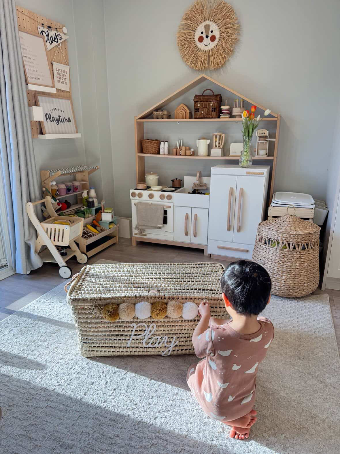 Enfant jouant avec un coffre à jouets personnalisé en osier brodé "Play" dans une chambre bébé au style Montessori et boho.