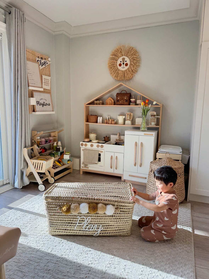 Toddler sitting next to a personalized boho wicker toy trunk to show the storage capacity and size for a nursery.